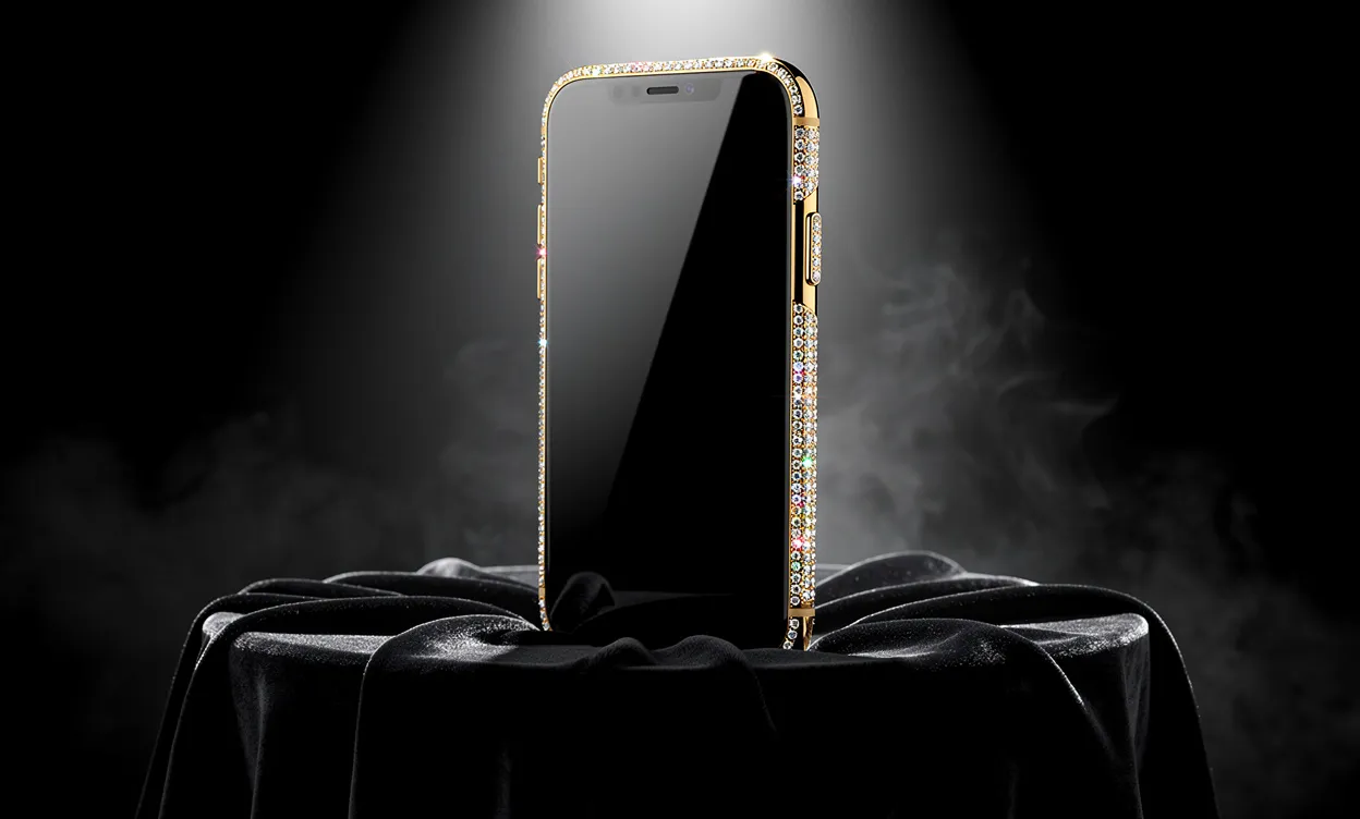 Un smartphone orné de diamants et d’or repose sur un piédestal en velours sous un éclairage intense.