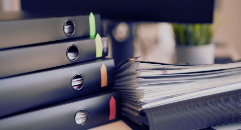 Pile de classeurs à anneaux avec marque-pages de couleur à côté d'une liasse de documents