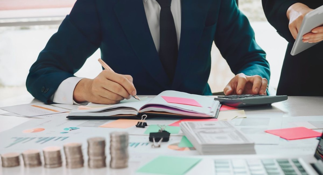 Comptable annotant un carnet à côté d'une calculatrice et de documents financiers sur un bureau